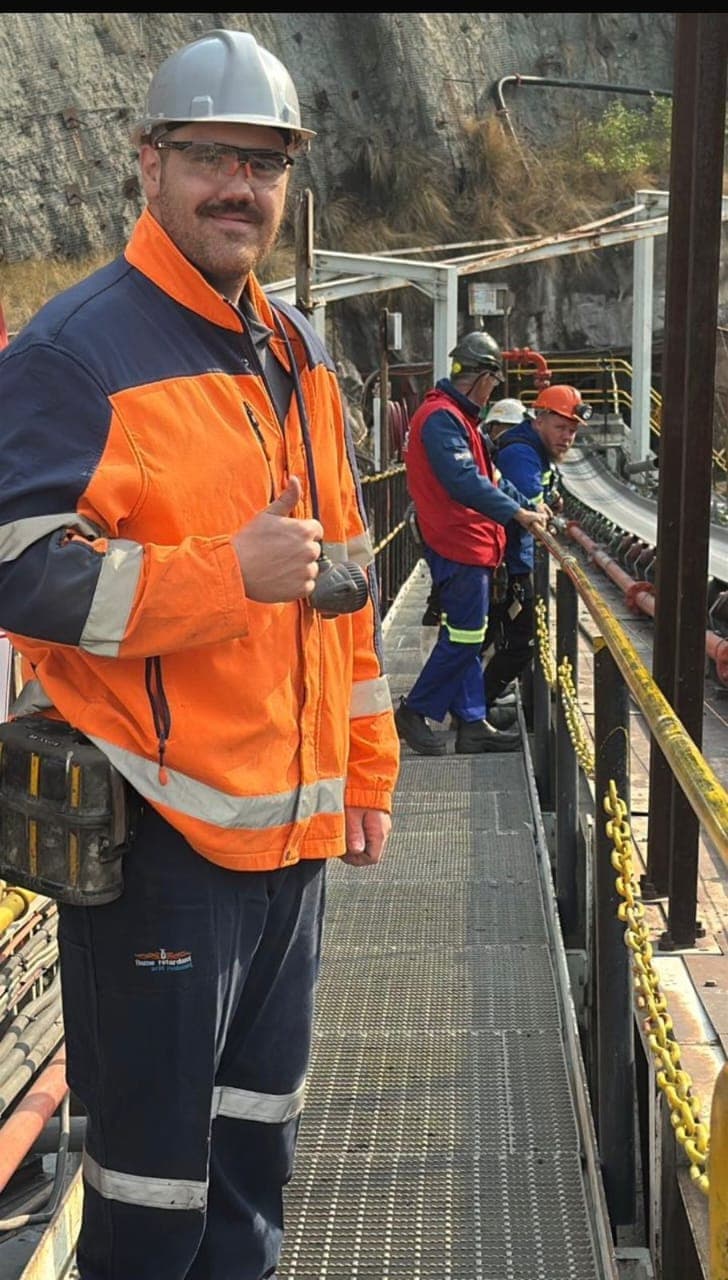 David from Kia-Kaha Mining on a mine plant walkway during a cable-jointing job, with the crew working on the cable behind him