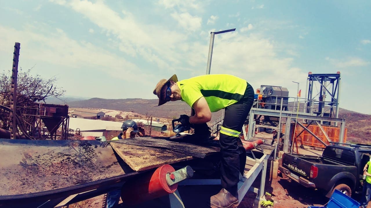 A Kia-Kaha Mining technician working on a stationary conveyor at a mine site, with the company vehicle in the background