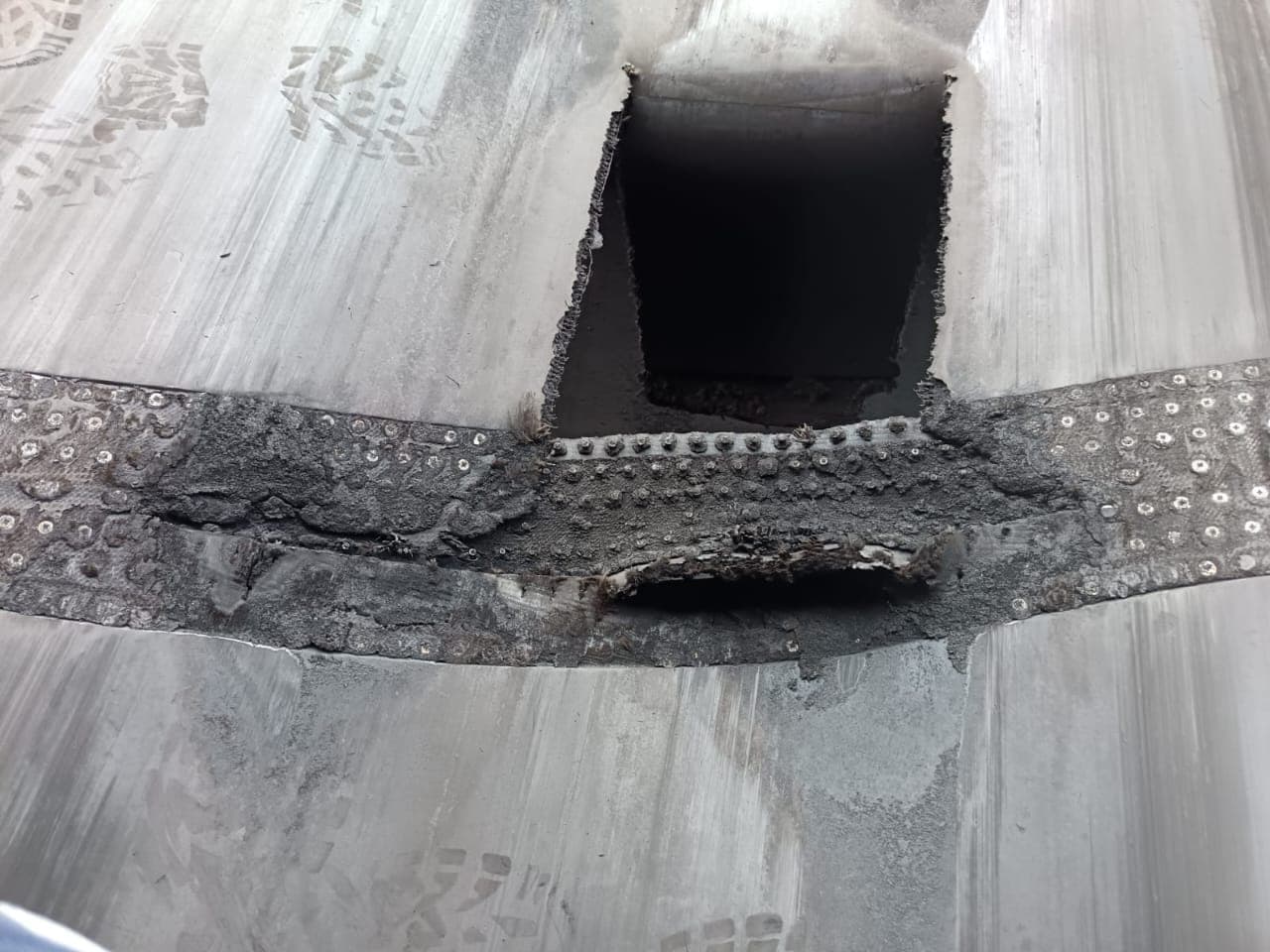 A conveyor belt splice with torn edges and exposed carcass fabric before repair